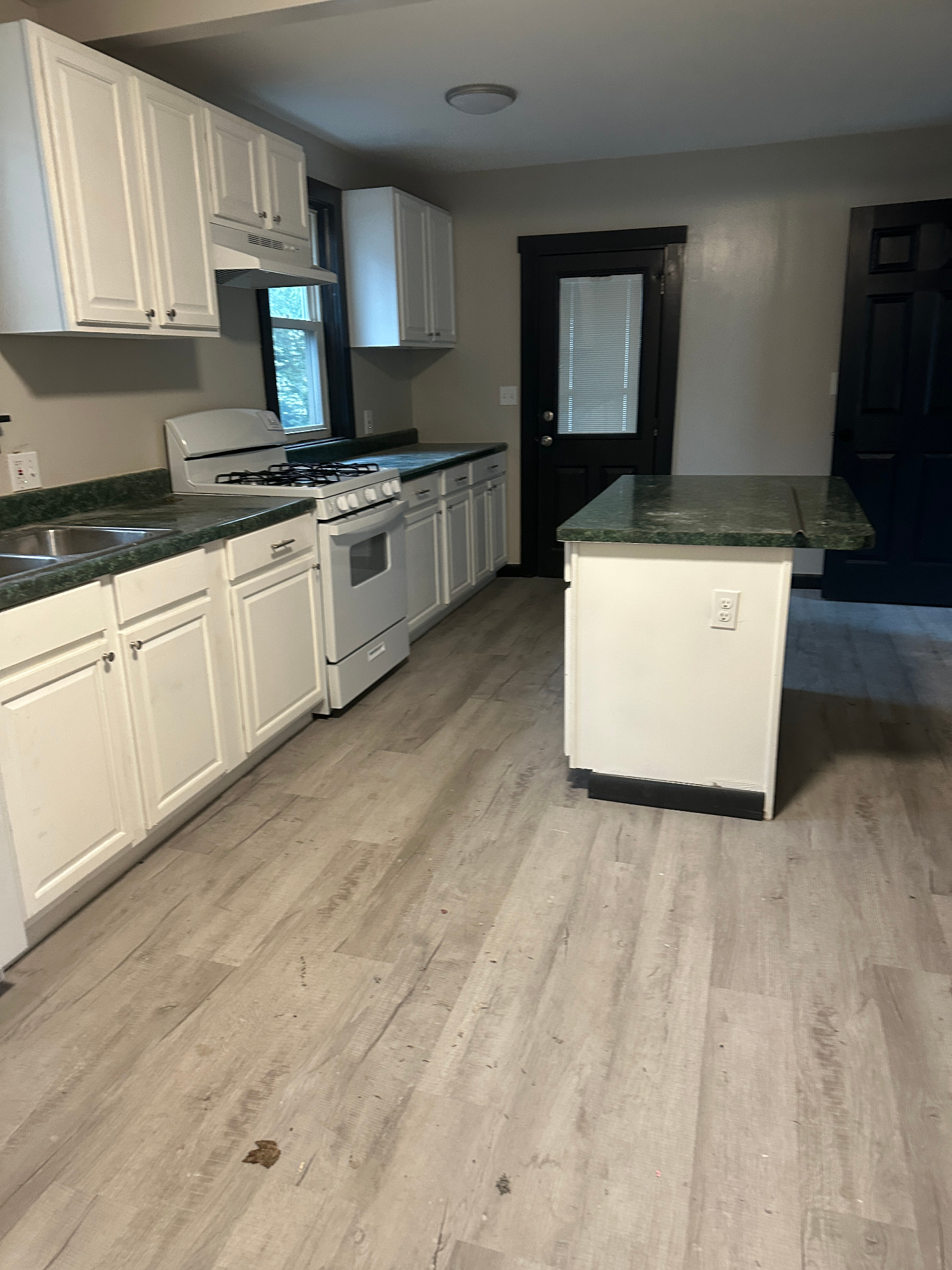 Renovated kitchen with new wood-look flooring, white cabinets, and island