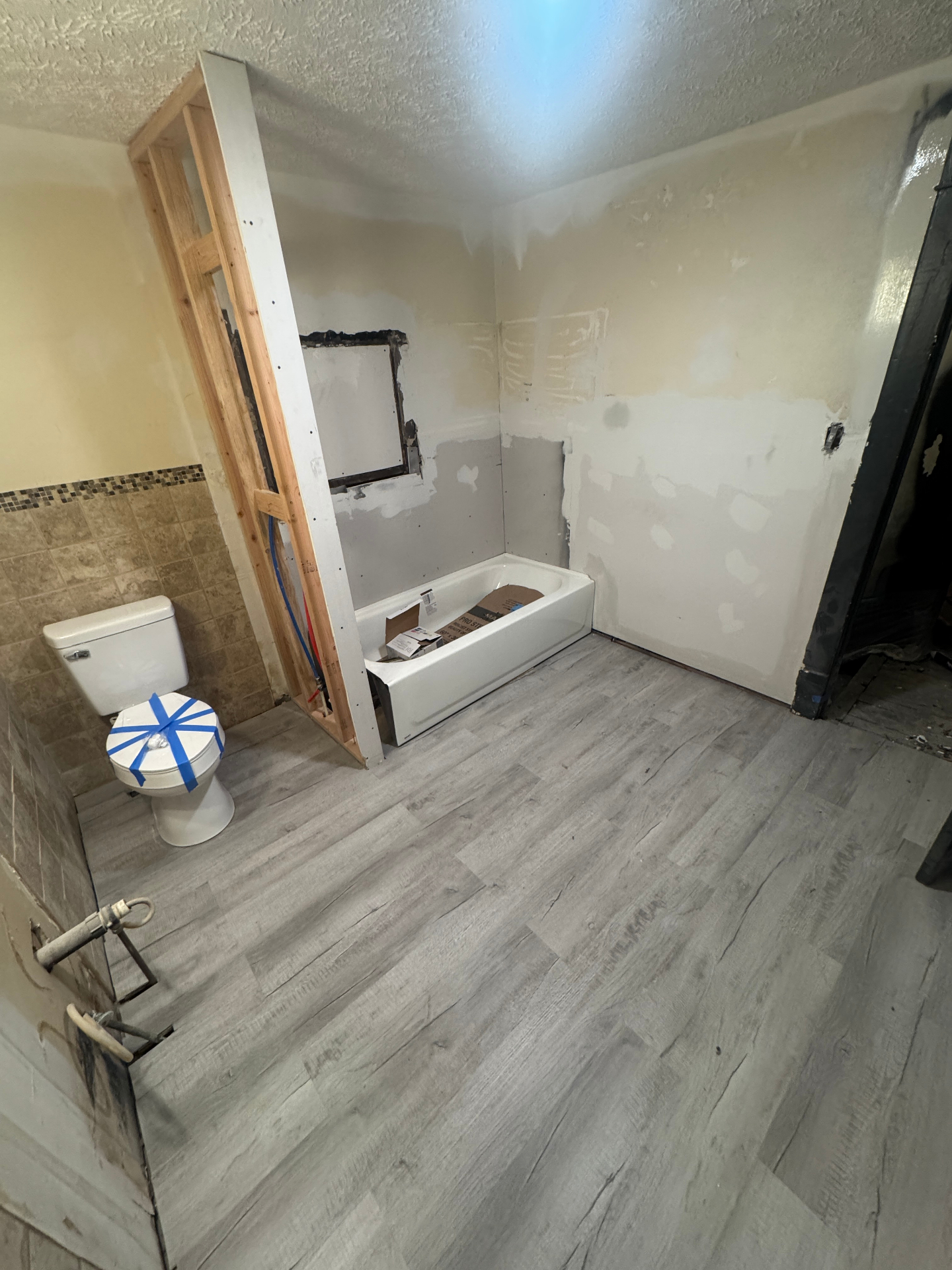 Bathroom mid-renovation with framed wall, exposed plumbing, and new tub set in place