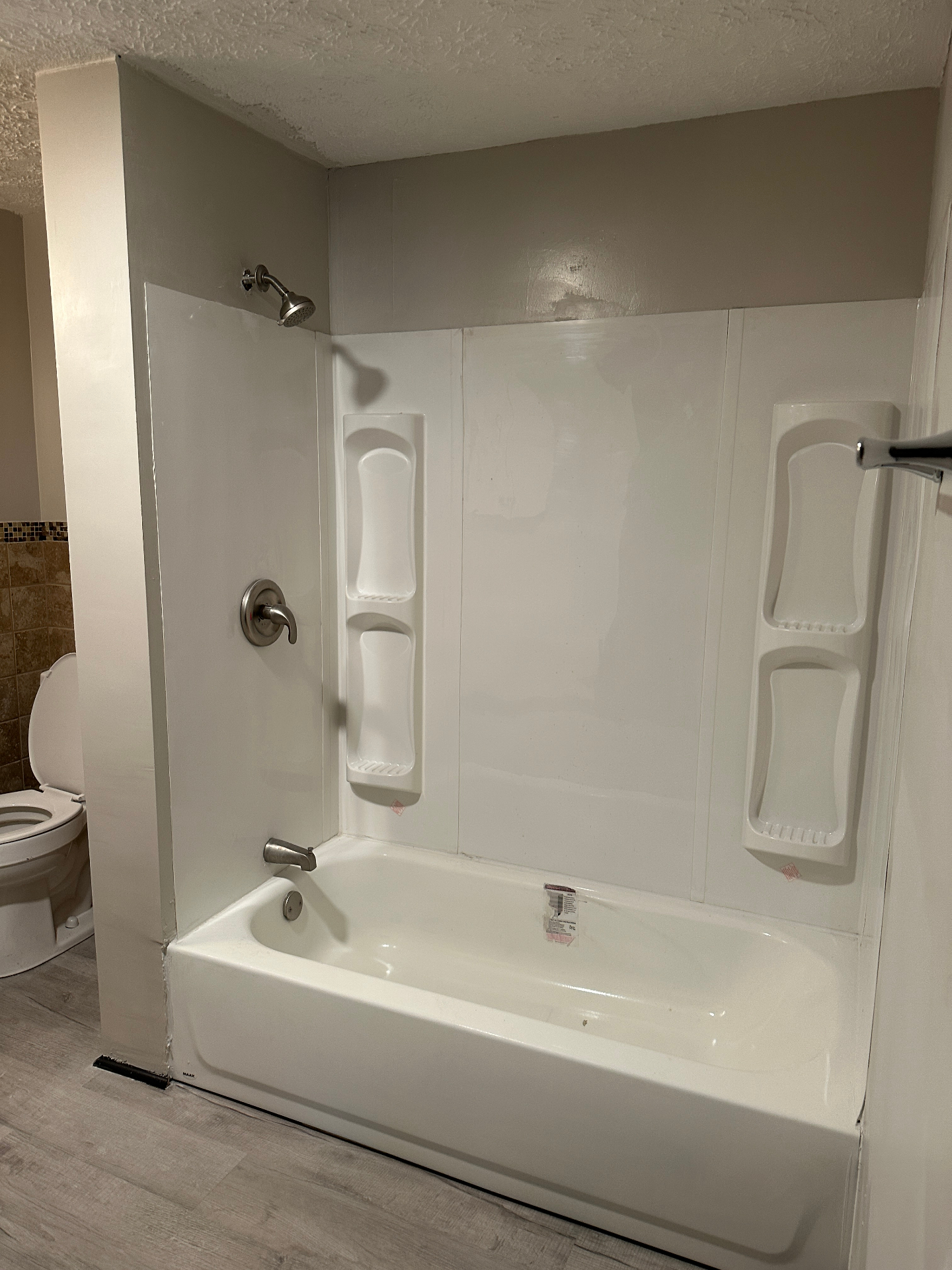 Finished bathroom with installed tub surround, shower fixtures, and clean walls